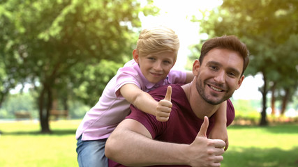 Father and son enjoying piggyback ride, showing thumbs up, support and trust