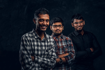 Studio photo. Portrait of a three Indian students wearing casual clothes against a dark textured wall.