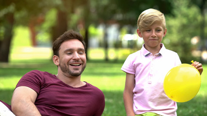 Joyful father and son blowing balloons for birthday party, fooling around, funny