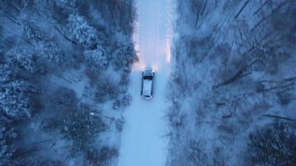 Tracking birdseye drone shot of SUV on snow covered rural road. Evening drive with headlights on, in Northern Ontario, Canada. Winter driving. - Powered by Adobe