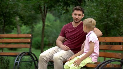 Father and son sitting on bench in park, men talks, spending time together