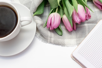 Woman working desk with coffee mug, notebook and spring pink bouquet of tulip flowers, feminine flat lay style