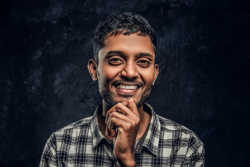 Fototapeta premium Portrait of a young Indian guy wearing a checkered shirt holding hand on chin, smiling and looking at a camera in a studio 