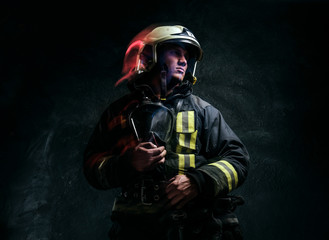 Studio portrait in a dark studio against a textured wall. Brutal firefighter in uniform and safety...