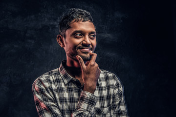 Portrait of a handsome young Indian guy wearing a checkered shirt holding hand on chin and looking sideways with a pensive look