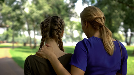 Fototapeta premium Back view of mum and daughter walking in park, conversation about life, advising