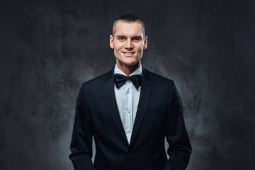 Portrait of a handsome stylish wearing elegant classical suit with a bow tie. Studio shot on a dark textured wall