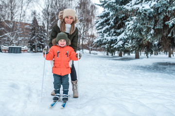 Young mother woman holds a little boy 2-3 years old, son in winter clothes. In the winter in the woods in the resort rest. Free space for text. Care and safety of the child in the family.