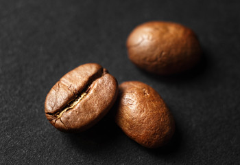 Three roasted coffee beans on black paper background. Shallow depth of field. Selective focus.