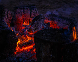 there are red coal and fire flames in the middle of the campfire, but there are big, burning ash blocks around