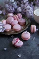 Fototapeta na wymiar Lavander or blueberry macarons with vanilla ganache on vintage silver plate and dark stone table, decorated with lilac flowers