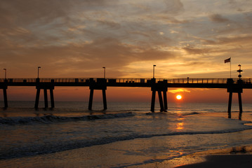 Fototapeta na wymiar Sun setting under the pier in Destin, Florida, while waves crash onto the beach