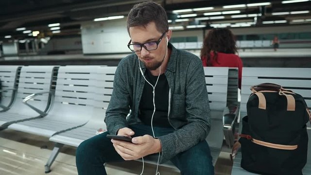 Adult man is waiting a train in underground, listening to music by headphones