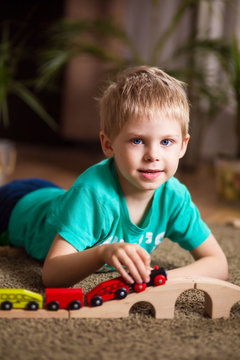 happy baby, blonde with blue eyes, a little boy of five years in the mint (green / blue) t-shirt in shorts barefoot near the couch in the apartment igret fun with wooden railway