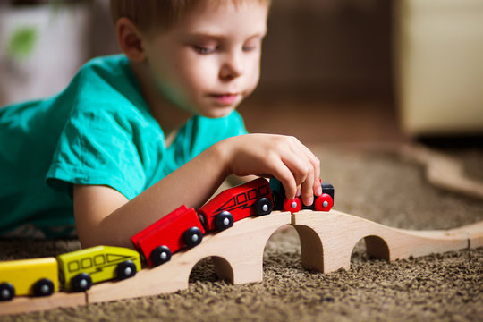 happy baby, blonde with blue eyes, a little boy of five years in the mint (green / blue) t-shirt in shorts barefoot near the couch in the apartment igret fun with wooden railway