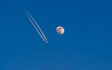 Image of airplane with condensation trails flying next to the detailed moon