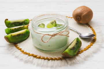 Yogurt with kiwi slices on a wooden white background.