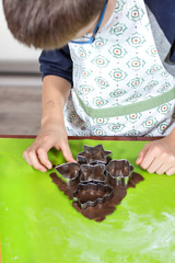 Dłonie chłopca wyciskającego kształty z metalowych foremek z ciasta położonego na zielonej...