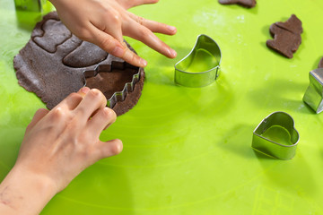 Dłonie chłopca wyciskającego kształty z metalowych foremek z ciasta położonego na zielonej silikonowej stolnicy. Zajęcia kulinarne dla dzieci.