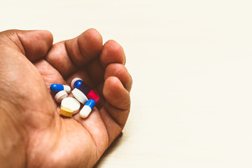 Medicine capsules (assorted pills) in a man's hand. Light background. Concept of self-medication, health, depression, cancer, medications.