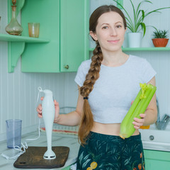 Woman holding celery stalk and immersion blender in stylish minimal kitchen. Healthy lifestyle...