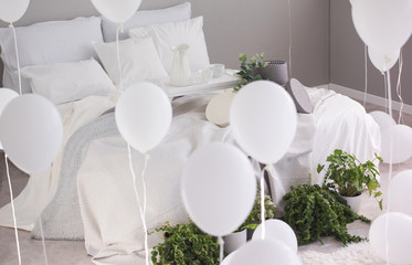 Urban jungle and bunch of white balloons in trendy bedroom with king size bed with white bedding and grey blanket