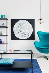 Blue egg chair in bright living room with black metal furniture and moon graphic on the wall, real photo