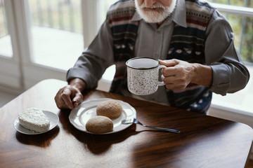 Lonely senior man sitting at kitchen table drinking tea