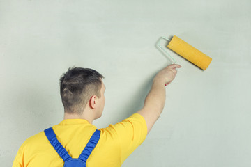 The repairman treats the wall with a primer using a roller. Light photo .