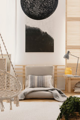 Abstract black and white painting on the wall in bright bedroom interior with futon bed and vase and lamp on bedside table
