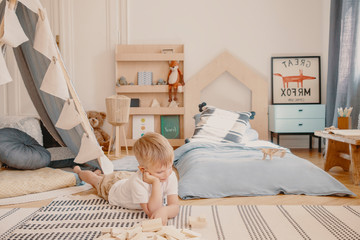 Cute little boy laying on the floor of his stylish scandinavian bedroom, real photo