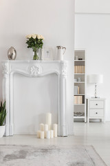 Flowers on elegant portal above candles in white apartment interior with grey carpet. Real photo