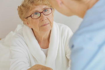 Worried elderly woman suffering from osteoporosis looks at daughter who visited her at the hospital
