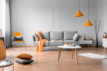 Fashionable living room interior design with grey couch, wooden coffee table and orange accents