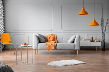 Orange accents in grey living room interior with copy space on empty wall