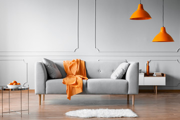 Orange blanket on grey scandinavian sofa, copy space on grey living room wall
