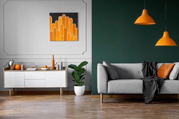 Abstract orange painting on grey wall of stylish living room interior with white wooden furniture...