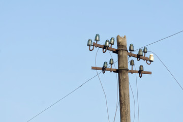 Old electric  wooden pole with glass and ceramic insulators and electric wires against blue sky....