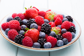 Fresh berry salad on blue dishes. Vintage wooden background.