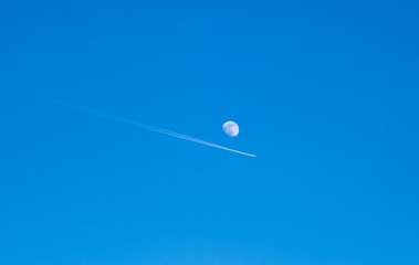 Image of airplane with condensation trails flying next to the detailed moon