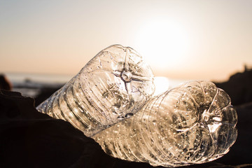 Plastic bottles are lying on a stone by the sea at the golden hour. Environmental problem concept