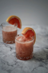 Two cold drinking glasses with fresh grapefruit summer alcohol cocktail. Gin and tonic with red grapefruit on wooden background.