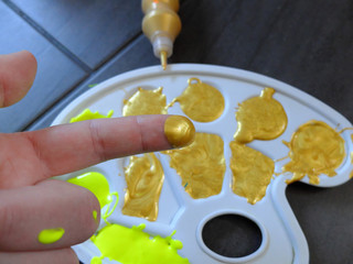 Artists plastic palette with large amounts of yellow and gold colors on the floor with man's hand taking small amount of gold paint for finger painting