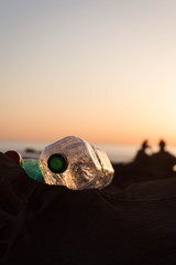 plastic bottles lie on a stone by the sea against the sunset sky and the silhouette of people. golden hour. Concept of pollution, creative background.