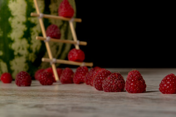 Watermelon house for raspberries. Ladder of chopsticks. Close-up, black background, isolated, place for text.