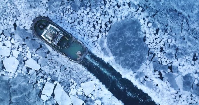 Top aerial view of tug boat floating through ice floes of winter Eastern Bosphorus strait. Vladivostok, Russia. Evening