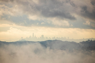 Break between fog and clouds reveals distant San Francisco skyline in sunrise glow