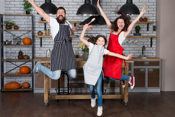 Having fun in kitchen. Family mom dad and little daughter wear aprons jump in kitchen. Family having fun cooking together. Teach kid cooking food. Weekend breakfast. Cooking with child might be fun