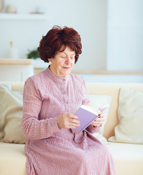 portrait of beautiful mature woman (80 years old) sitting on sofa at home, reading a book with great-grandson