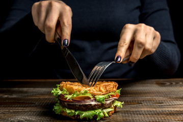 Healthy lifestyle, proper nutrition. Female hands cut a useful rice burger with vegetables, herbs and cutlet on a wooden board